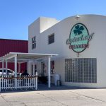 Buhl ID 11 A white building with a large “CloverLeaf Creamery” sign, outdoor seating under a pergola, and a red building in the background, on a sunny day. A tall ice cream cone sculpture stands near the street.