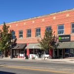 Buhl ID 15 A two-story brick building houses several businesses, including H&R Block. Trees line the sidewalk and a white van is parked on the street under a clear blue sky.